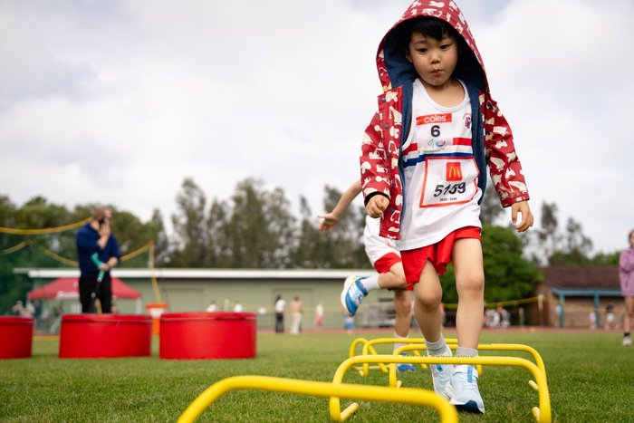 An athlete in a raincoat going over the hurdles